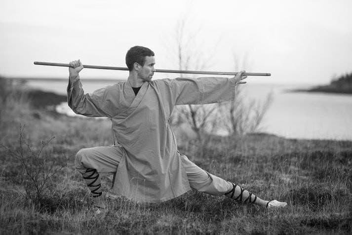 Gísli in a low stance with a staff by the sea